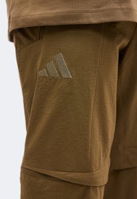 Shorts marron texturé avec une petite poche latérale et un logo brodé comportant trois barres diagonales sur la cuisse gauche.