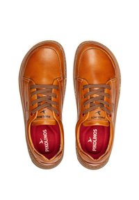 Zapatillas de cuero marrón con un acabado suave, puntera redondeada, detalles de costura, diseño de cordones y plantillas rojas en contraste.