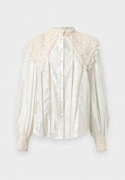 Blusa bianca con colletto in pizzo, maniche a sbuffo e intricate fantasie floreali. Chiusura frontale con bottoni e dettagli in pizzo sui polsini.