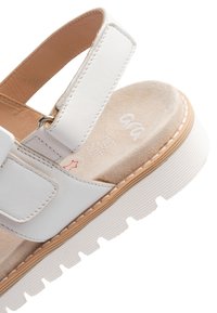 White leather sandal with a padded top strap, adjustable buckle, and textured beige insole. Features a ridged white sole with brown accent.