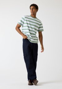 Gestreiftes, kurzärmliges T-Shirt in Grün und Weiß mit besticktem Logo, kombiniert mit dunklen Cargo-Jeans mit seitlichen Taschen und lässiger Passform.