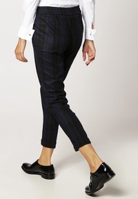 Czarne spodenki w pepitkę o luźnym kroju, z elastycznym paskiem w talii i mankietami na kostkach, w zestawieniu z błyszczącymi czarnymi butami.