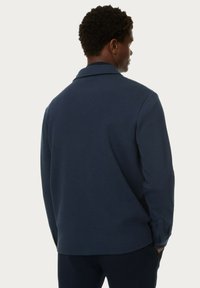 Camicia colletto di un blu navy scuro, realizzata in un tessuto morbido, caratterizzata da maniche lunghe e una vestibilità rilassata. La vista posteriore mostra un design senza cuciture e dettagli minimi.