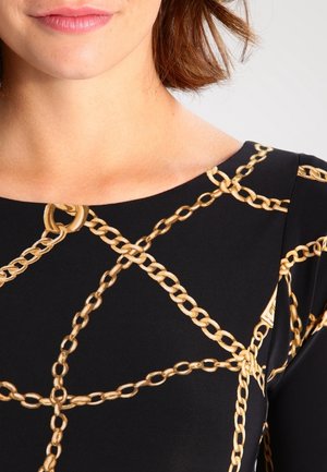 Sort stoftop med et guld kædemønster. Designet inkluderer geometriske former og detaljer, med en rund halsudskæring og tætsiddende silhuet.