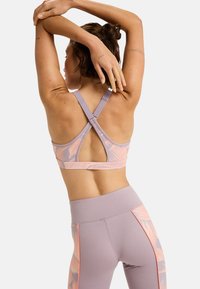 Reggiseno sportivo di un leggero viola con motivi di foglie rosa, dotato di un design a schiena scoperta e spalline regolabili. La zona del busto presenta una costruzione senza cuciture.