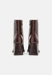 Bottines en cuir imprimé croco marron avec une finition brillante, bout carré, talon carré de hauteur intermédiaire et fermeture éclair sur le côté.