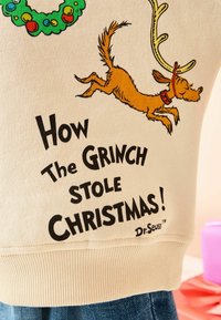 Béžová mikina s nápisom "Ako Grinch ukradol Vianoce!" v čiernej farbe, s hnedým kresleným psom v parohoch a s červeným obojkom.