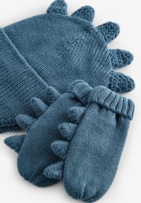Eine gestrickte Mütze und passende Fäustlinge aus strukturiertem blauen Garn. Die Mütze hat verspielte, spitze Akzente. Die Fäustlinge besitzen gerippte Bündchen und Spitzen.