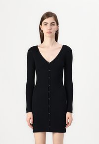 Robe noire côtelée avec décolleté en V, manches longues et fermeture à boutons sur le devant. Le tissu a un aspect texturé et un design ajusté.