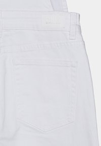 Zadní pohled na bílé denimové džíny, které ukazují prošité zadní kapsy, poutka na opasek a nenápadnou značkovou etiketu na pase.