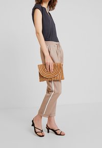 Marinblå topp med polka prickar, beige byxor med elastisk midja och vita sidostrick, samt en texturerad gyllenbrun clutchtaske med böljande mönster. Svarta strap-on klackar.