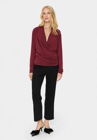 Maroon garšraksts ar garām piedurknēm un izplūdušām detaļām, pārī ar melnā krāsā taisnām biksēm. Modelis valkā melnas augstpapēžu čības ar lentīšu akcentiem.