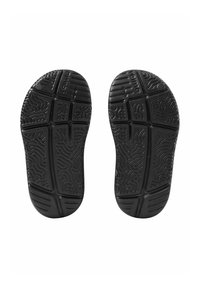 Semelles de chaussures en caoutchouc noir avec des motifs texturés, comprenant des rainures et des crêtes pour la traction, présentées en vue de dessus.