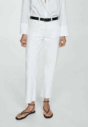 Bele straight-leg jeans z raztrganim robom, v kombinaciji z črnim pasom; obuti so črne thong sandale. Majica je bela in dolgimi rokavi.