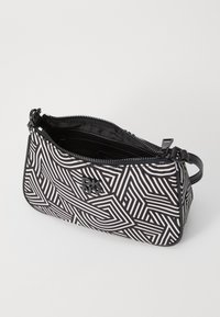 Borsa in bianco e nero con motivo geometrico, chiusura con zip, esterno testurizzato e manico piccolo; presenta il logo DKNY sul lato.
