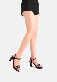 Sandali neri con tacco alto, caratterizzati da un design aperto sulla punta, sottili cinturini, dettagli metallici e una finitura testurizzata sulla parte superiore.