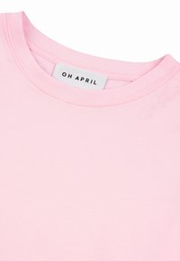 Lyserød crewneck-trøje med mærket "OH APRIL" syet ind i kraven og diskret broderet tekst nær halsudskæringen.