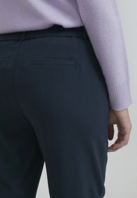 Námořnické kalhoty s hladkým povrchem a rovnou siluetou, obsahující zadní kapsu a diskrétní design pasu, ve spojení se svetrem světle fialové barvy.