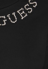 Sudadera negra con la palabra "GUESS" adornada con brillantes plateados a lo largo del escote, de textura suave y con tejido acanalado.