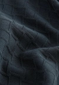 Tissu gris foncé avec motif en zigzag et losanges tricotés en relief, montrant des plis et des détails de texture.