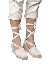Scarpe espadrillas beige con tacco a zeppa, dotate di fasce incrociate in tessuto. Il design presenta una suola in juta testurizzata e una parte superiore in tela morbida.