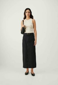 Hvit ermeløs topp med rund hals, parret med et høyhøydet svart denimskjørt. Modellen holder en liten svart håndveske. Sorte ballerinasko.