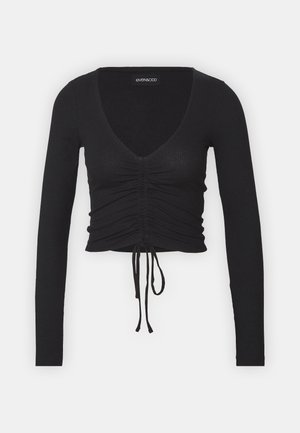 Black ribbed long-sleeve crop top featuring a deep V-neck, gathered detailing at the front, and adjustable tie at the hem.