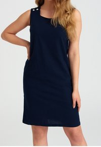 Námořnické bezrukávové šaty s kulatým výstřihem, bočními kapsami a dvěma dekorativními stříbrnými knoflíčky na levém rameni. Hladká, strukturovaná tkanina.