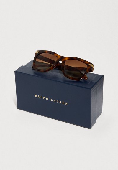 Γυαλιά ηλίου με σχέδιο χελώνας, σκούρους φακούς, γωνιώδες σχήμα και χρυσές λεπτομέρειες. Συνοδεύονται από ένα ναυτικό μπλε κουτί με χρυσά γράμματα.