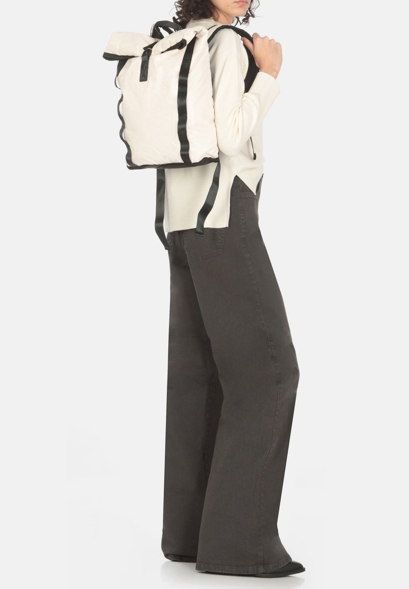 Zaino in tessuto bianco con spallacci neri, forma rettangolare e finitura testurizzata. Design con parte superiore arrotolata, fissata con dettagli in metallo nero.