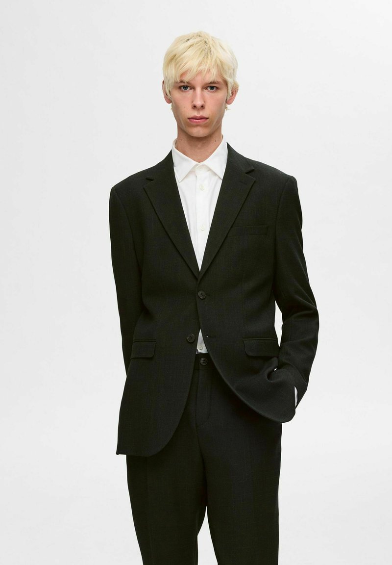 Ciemnoszary żakiet i pasujące spodnie, z klapami, dwoma guzikami i kieszeniami z przodu. Biała koszula pod spodem dopełnia całość.