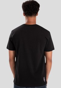 Camiseta de algodón negra con mangas cortas, cuello redondo y un pequeño diseño bordado en la parte inferior derecha. Textura suave y corte relajado.