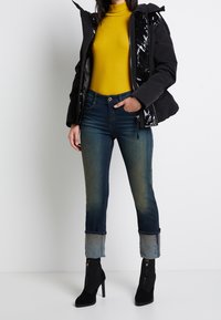 Svart puffjacka med glänsande foder, gul halsduk, och högmidjade blå jeans med uppvikta benslut samt svarta vadboots.