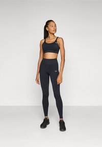 Ensemble de sport noir comprenant un haut court et un legging taille haute, avec une texture lisse et des coutures minimales. Chaussures de sport noires.
