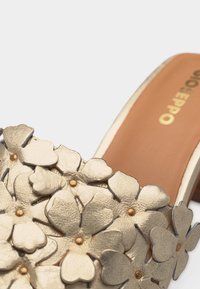 Σανδάλι με ανοιχτά δάχτυλα διακοσμημένο με χρυσές μεταλλικές ανθοδέσμες και ταμπά πάτο με χρυσό λογότυπο.