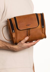 Brown leather bag with zippered compartments, a flap closure, and a side handle. Smooth texture with stitching details and logo.