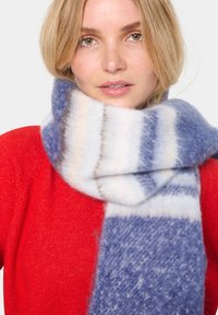 Uldblandingshalstørklæde med blå og hvide striber og blød tekstur, viklet om halsen, suppleret med en rød sweater.