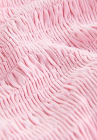 Țesătură roz cu o textură strâns adunată, plisată, creând pliuri orizontale mici și uniforme pe toată suprafața.