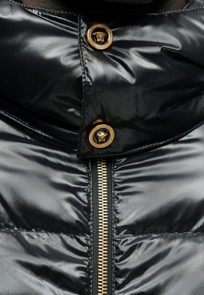 Sort puffjakke med en blank finish, der har en guldzips og guldløveemblembesatte knapper ved kraven og slåen.