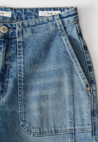 Jean en denim bleu clair avec une taille haute, un design à cinq poches et une fermeture à bouton en métal. Texture usée et accents cousus présents.