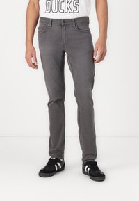 Jeans in denim grigio con una vestibilità slim, cinque tasche e chiusura con bottone. Abbinati a sneakers nere con strisce bianche.