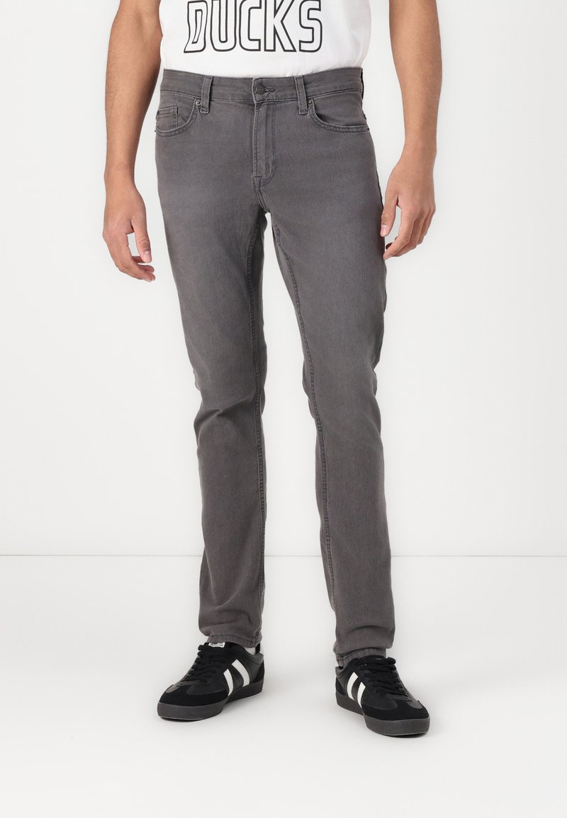 Jeans in denim grigio con una vestibilità slim, cinque tasche e chiusura con bottone. Abbinati a sneakers nere con strisce bianche.