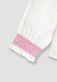 Weiße Bluse aus strukturiertem Stoff; gepuffte Ärmel enden in einem Rüschensaum mit rosa Smocking-Details.