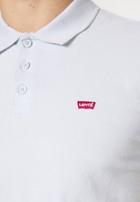 Světle modrá polo tričko vyrobené z texturované bavlny, s tříknoflíkovým zapínáním a malým červeným logem Levi's na hrudi.