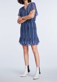 Kurzärmliges blau gestreiftes Kleid mit einem gerafften Saum, tailliertem Schnitt und transparenter Stoff. Kombiniert mit weißen Knöchelstiefeln und minimalistischen Design.