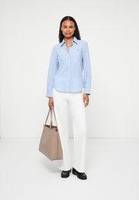 Blue and white striped button-up shirt with long sleeves, paired with white wide-leg pants. A beige tote bag and black loafers complete the look.