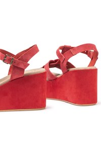 Red suede wedge sandals with a thick platform and crisscross straps featuring a metal buckle. Soft texture with a matte finish.