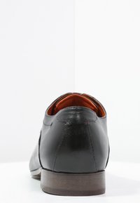 Chaussure en cuir noir à finition lisse, avec un bout rond et un intérieur orange contrastant. Elle présente un talon en bois marron et des accents de couture minimalistes.