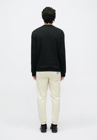 Juoda megztinis su ilgomis rankovėmis, žiūrint iš nugaros; derinamas su šviesiai smėlio spalvos laisvalaikio kelnėmis ir juodais batais. Paprastas dizainas be matomų raštų.