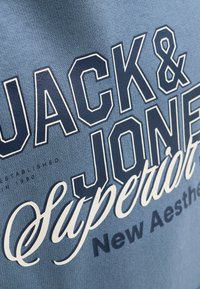 Μπλε ύφασμα με έντονα γράμματα που γράφουν Jack & Jones Superior και μικρότερο κείμενο που αναφέρει New Aesthetic.